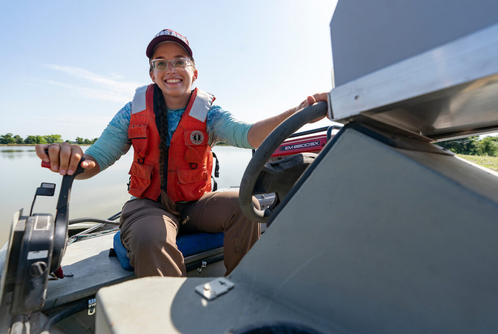 A girl driving a boat smiles at the camera.