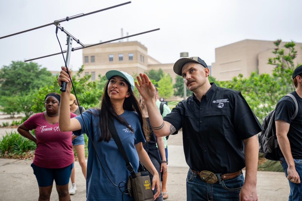 A student raises a metal antenna device above her head, while her teacher stands next to her