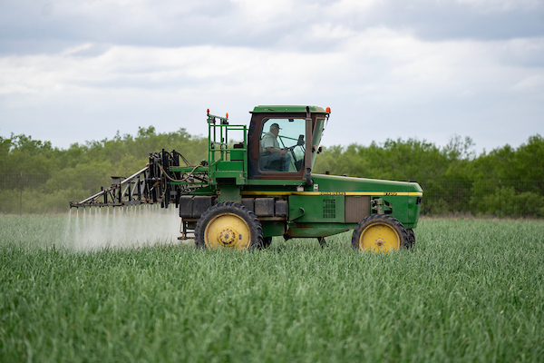 A man in a John Deer tractor sprays an agricultural field. 