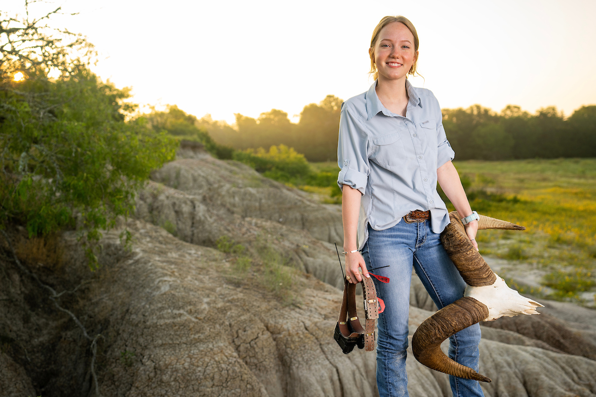 MacKenzie "Lulu" Hoffman standing on a rock holding a harness and the skull of a mountain goat
