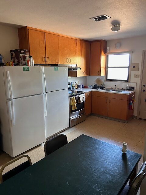 A dining and kitchen area with a table, two refrigerators, stove, sink and cabinets.